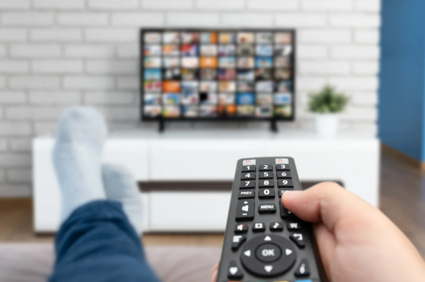 Viewer using a remote while comparing free streaming services cost through ads and upsells.